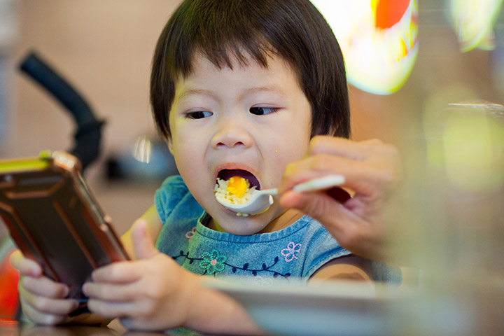 Mãe alimentando o filho enquanto o filho utiliza o celular